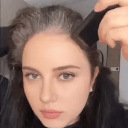 Person using a hairbrush on their hair with a neutral background