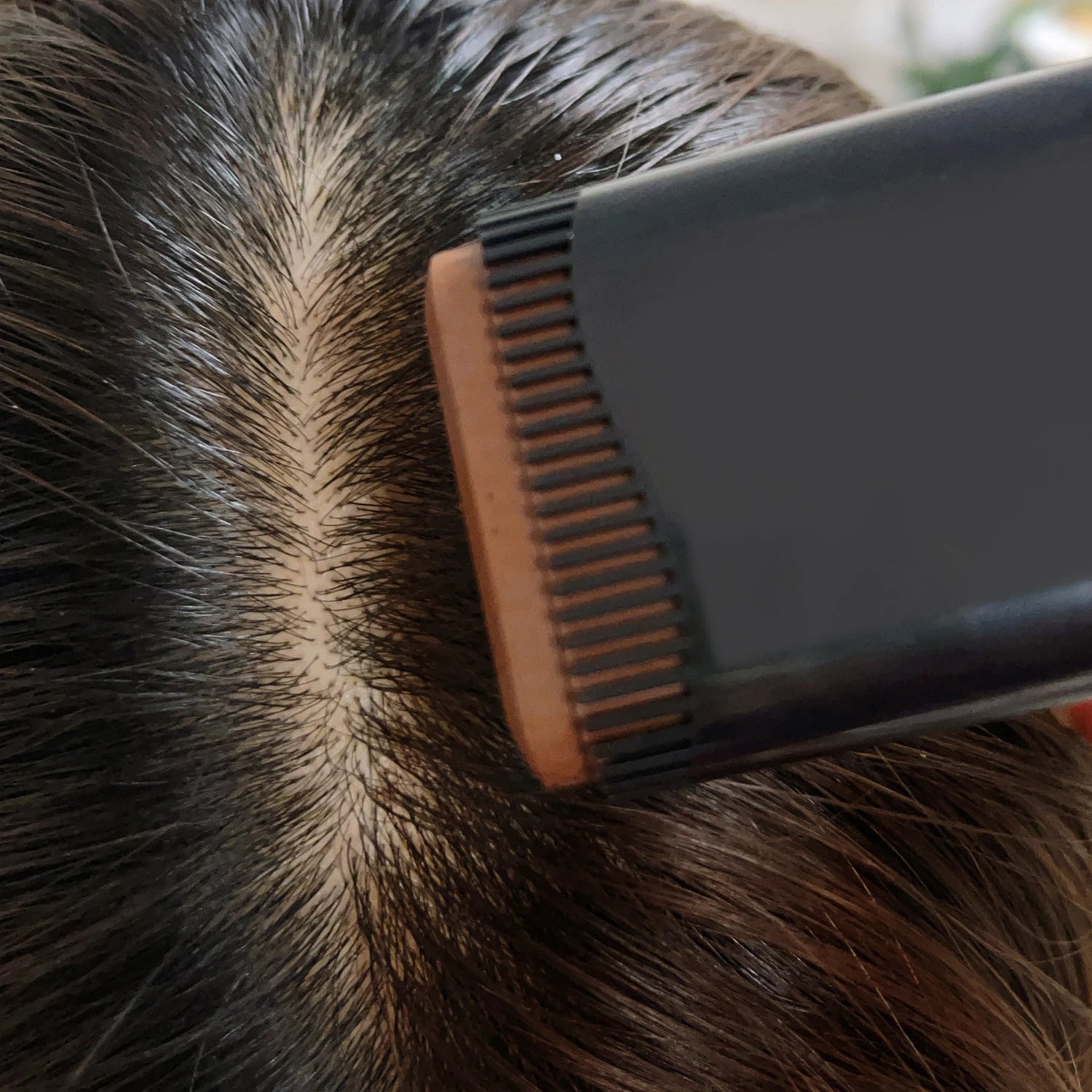 Person using a hairbrush on their head with a blurred background